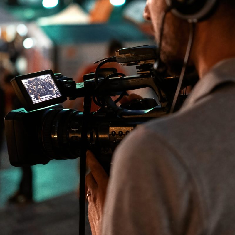 Professional cameraman recording poeple watching football in a public place at night